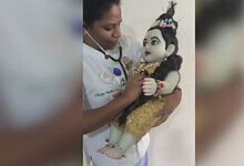 A woman holding a traditional puppet doll, dressed in ornate attire, in an indoor setting.
