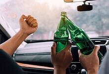 Celebrating with cheers and clinking green glass bottles inside a car during a festive occasion.