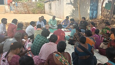 Women and children participating in a community meeting outdoors in a rural area.