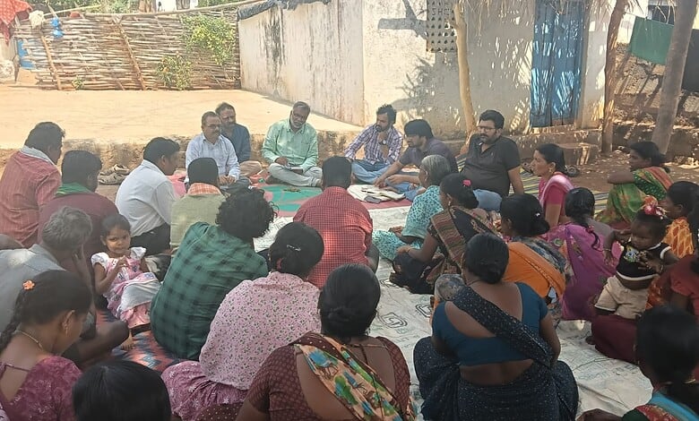 Women and children participating in a community meeting outdoors in a rural area.