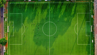 Aerial view of a well-maintained football pitch with players during a match, surrounded by a running trac.