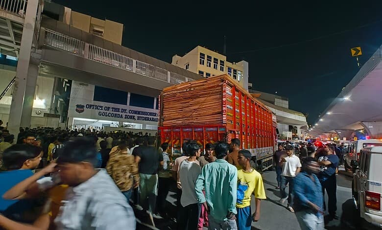 A busy street scene at night with a large red truck and a crowd of people in front of the Office of the D.