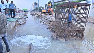 Flooded construction site with workers and machinery during heavy rain in an urban area.