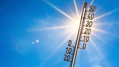 Thermometer showing high temperature with bright sun and clear sky in the background.