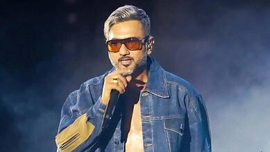 Male singer with sunglasses and denim jacket performing passionately on stage.