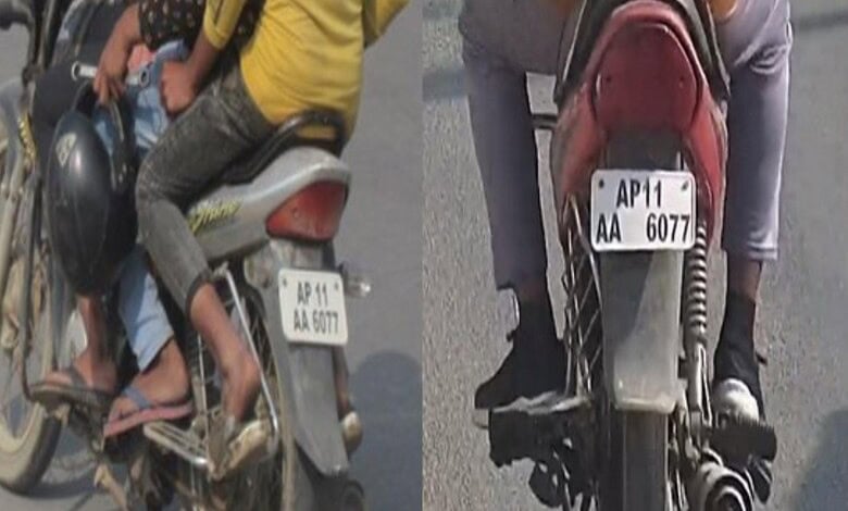 A man riding a motorcycle with a child sitting in front, both wearing helmets, on a busy street in India.