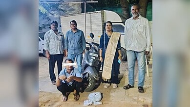 A woman and four men standing outdoors with a scooter and a small pile of stones in front of them.