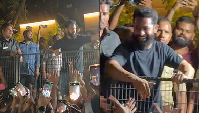A man smiling and greeting supporters at a public event, surrounded by fans taking photos and videos.