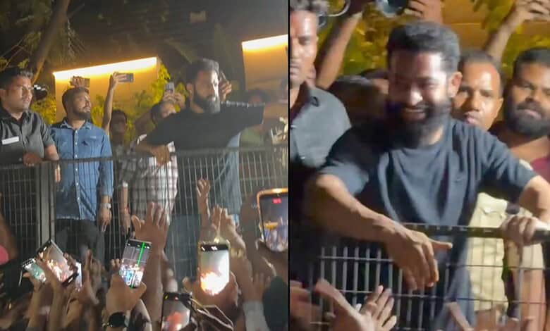 A man smiling and greeting supporters at a public event, surrounded by fans taking photos and videos.