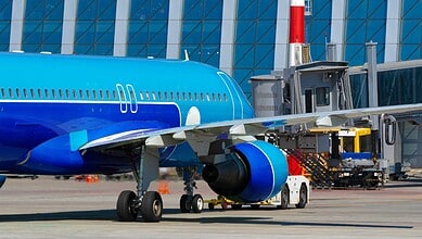 Commercial airplane at airport gate with jet bridge and ground support equipment.
