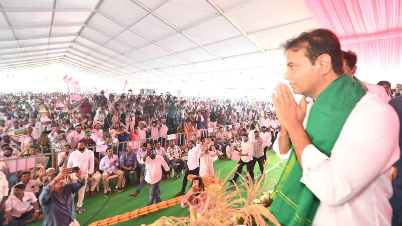 KTR praying with farmers at a large outdoor gathering under a tent.