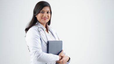 A woman doctor in a white coat holding a tablet, smiling confidently.