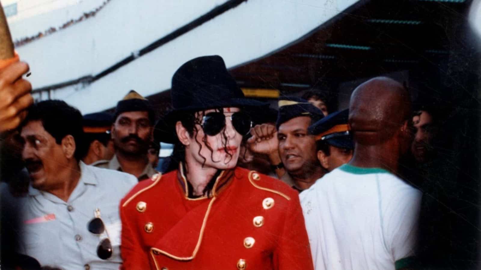 A woman dressed as Michael Jackson in a red jacket and black hat surrounded by a crowd at an event.