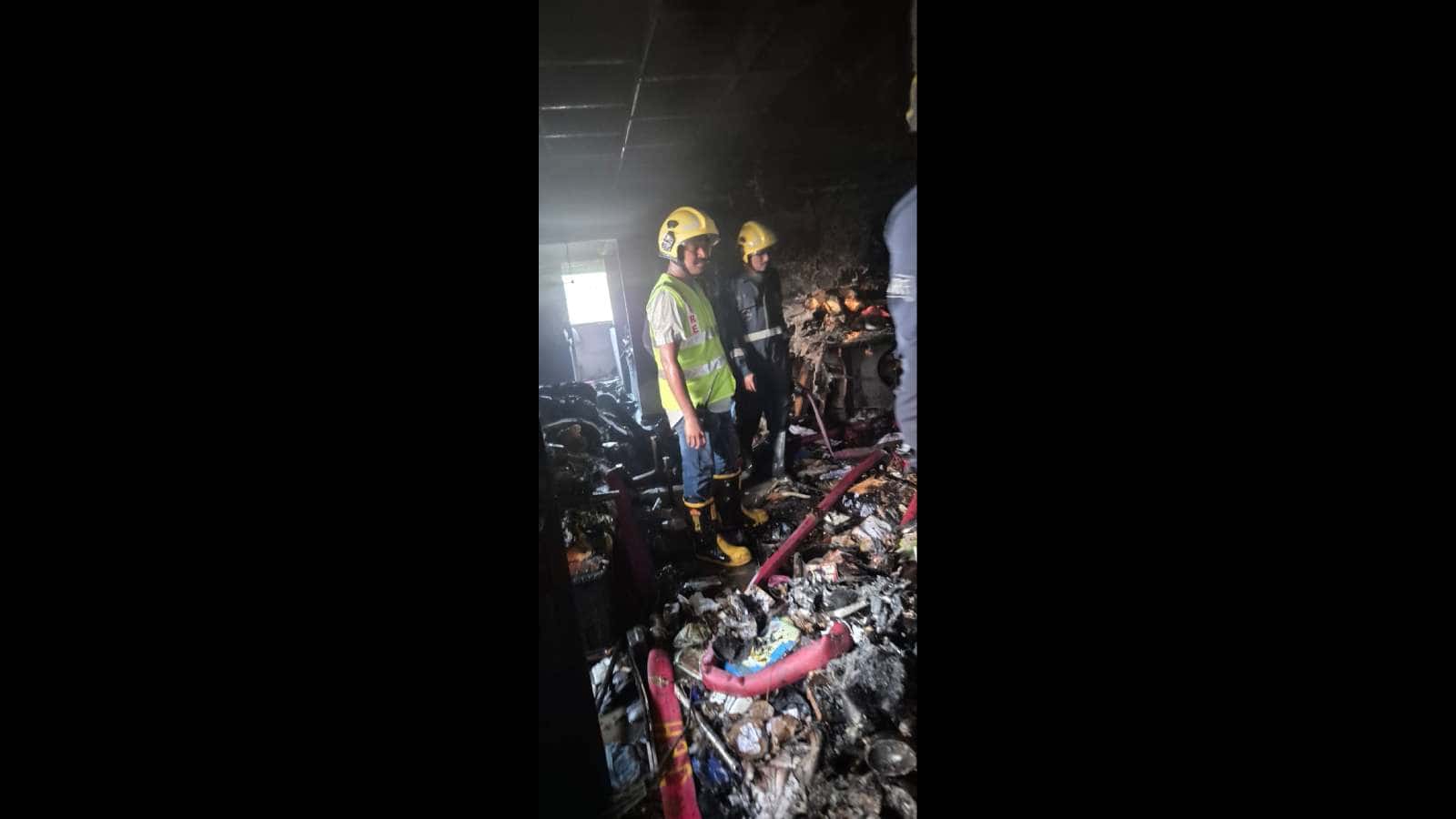 Firefighters inspecting the aftermath of a fire in a building filled with debris and burnt materials. Eme.
