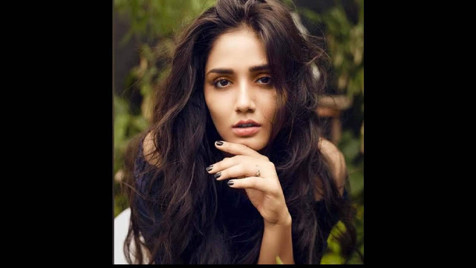 A woman with long, wavy dark hair posing outdoors in a natural setting.