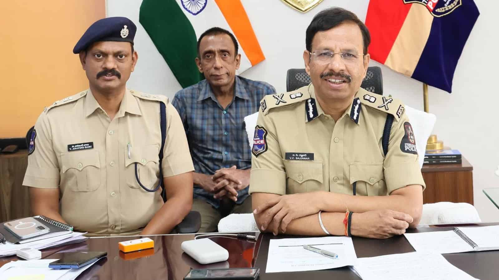 Police officers in uniform sitting at a desk with flags in the background, smiling during a formal meetin.