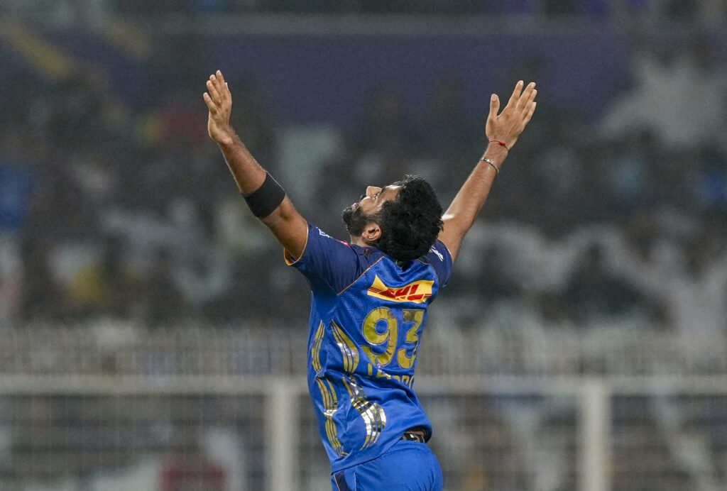 Celebrating cricket victory with player in blue jersey raising arms on the field.