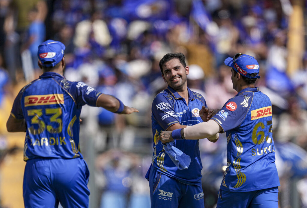 Excited cricket players celebrating on the field during a match with cheering crowd in the background.