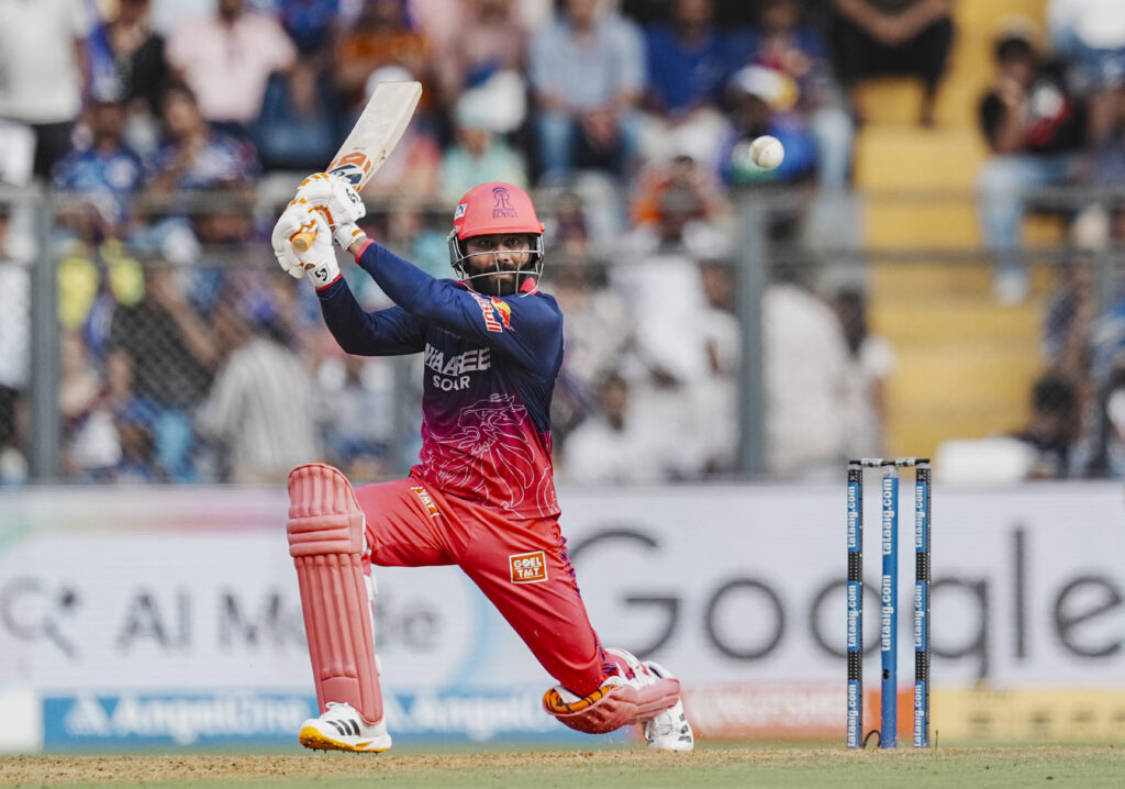 Cricket player in action during a match, batting with a helmet and pads on the field.