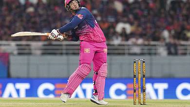 A woman cricket player in pink and blue uniform batting during a match on a cricket field.