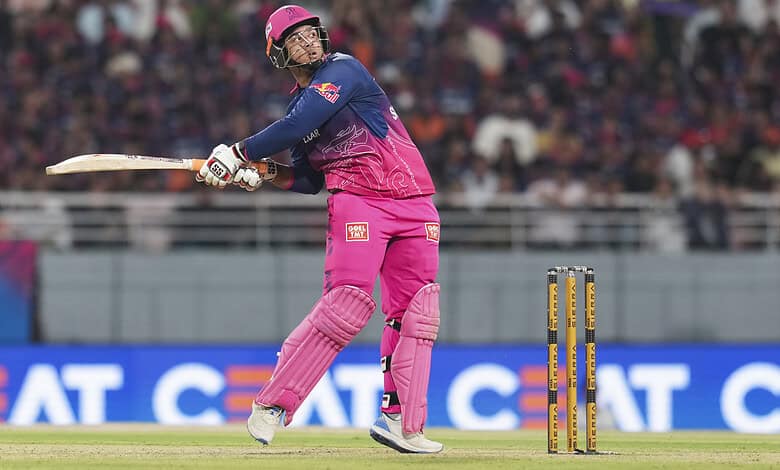 A woman cricket player in pink and blue uniform batting during a match on a cricket field.