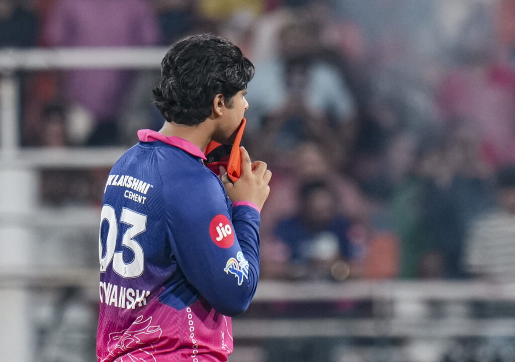 Young cricket player in blue and pink jersey holding a cricket bat during a match.