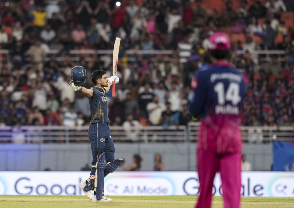 Indian cricket player celebrating after scoring a six during a match at a packed stadium.