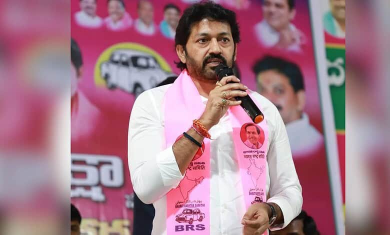 KCR speaking into a microphone during a political rally, wearing a pink scarf with images of leaders, in.
