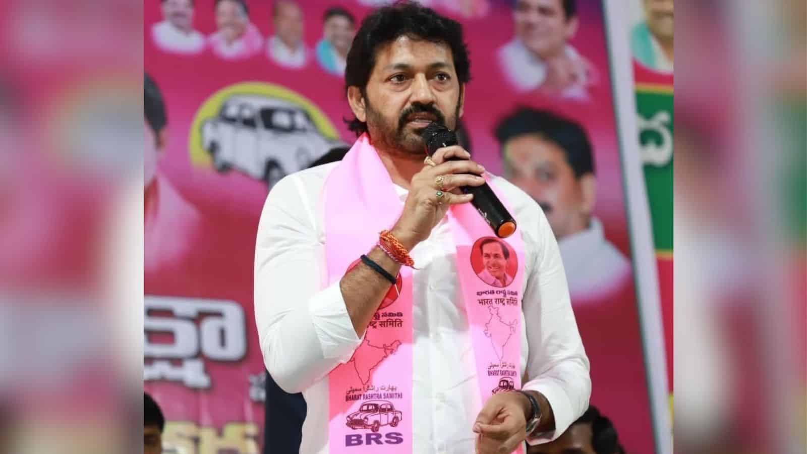 KCR speaking into a microphone during a political rally, wearing a pink scarf with images of leaders, in.