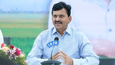 Indian Agriculture Minister speaking at a press conference outdoors with a microphone and flowers in the.