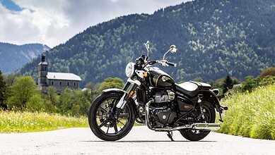 Classic black Royal Enfield motorcycle parked on a mountain road with lush green hills and a church in th.