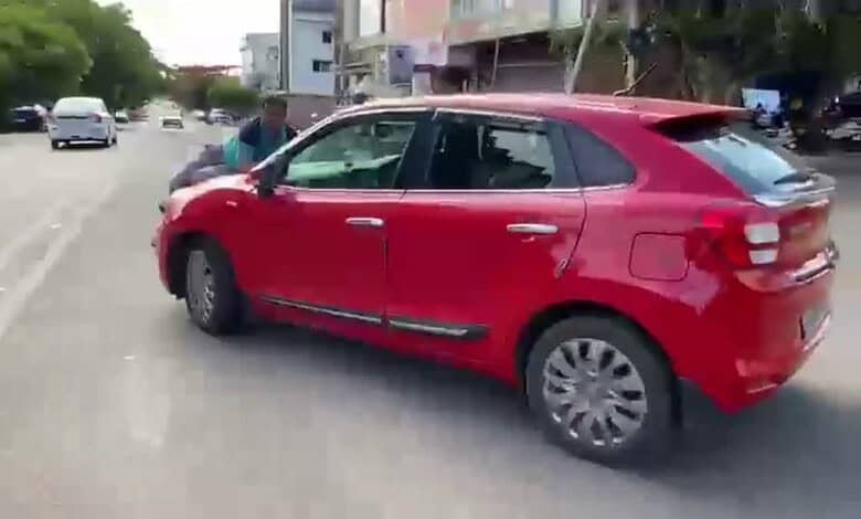 A red hatchback car parked on a city street with pedestrians and buildings in the background.