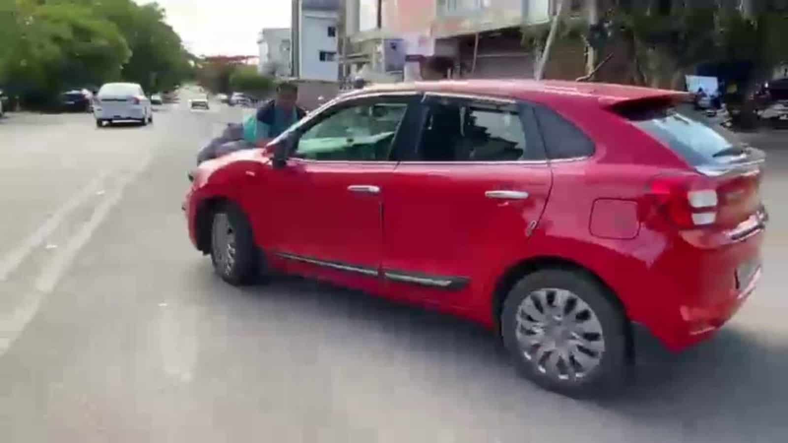 A red hatchback car parked on a city street with pedestrians and buildings in the background.