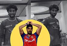A young male athlete in a sports jersey with a serious expression, standing indoors with elegant chandeli.