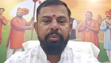 A man with a beard and traditional attire in front of a colourful Independence Day mural featuring histor.