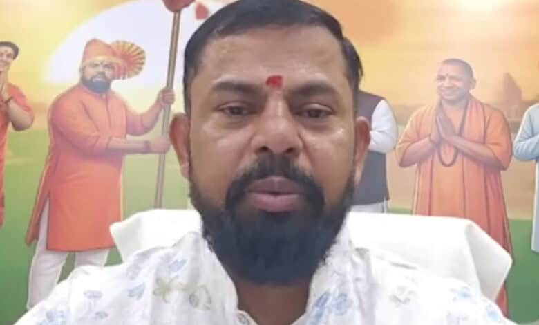 A man with a beard and traditional attire in front of a colourful Independence Day mural featuring histor.