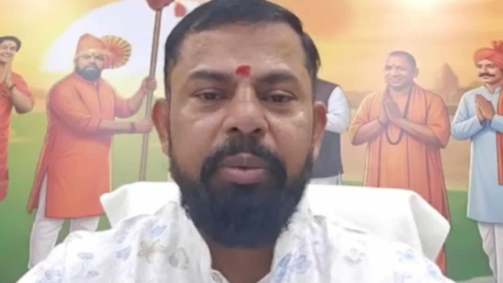 A man with a beard and traditional attire in front of a colourful Independence Day mural featuring histor.