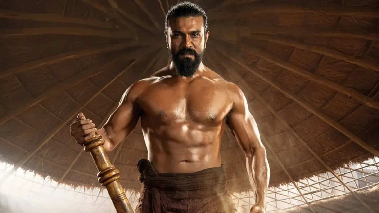 A muscular man with a beard holding a wooden stick in a traditional setting.