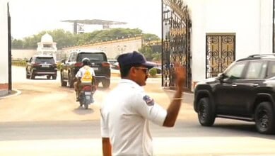 Security officer managing vehicle movement at entrance gate with parked cars and a motorcycle.