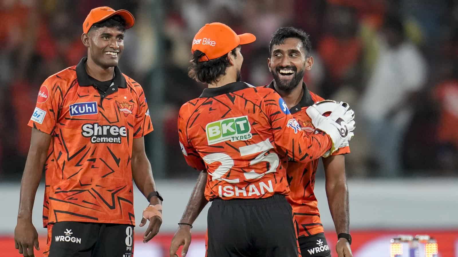 Excited cricket players celebrating victory during a match in vibrant orange uniforms.