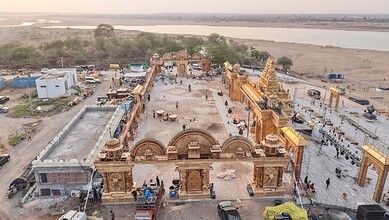 Ancient temple complex with intricate architecture and sculptures, set against a river and open landscape.