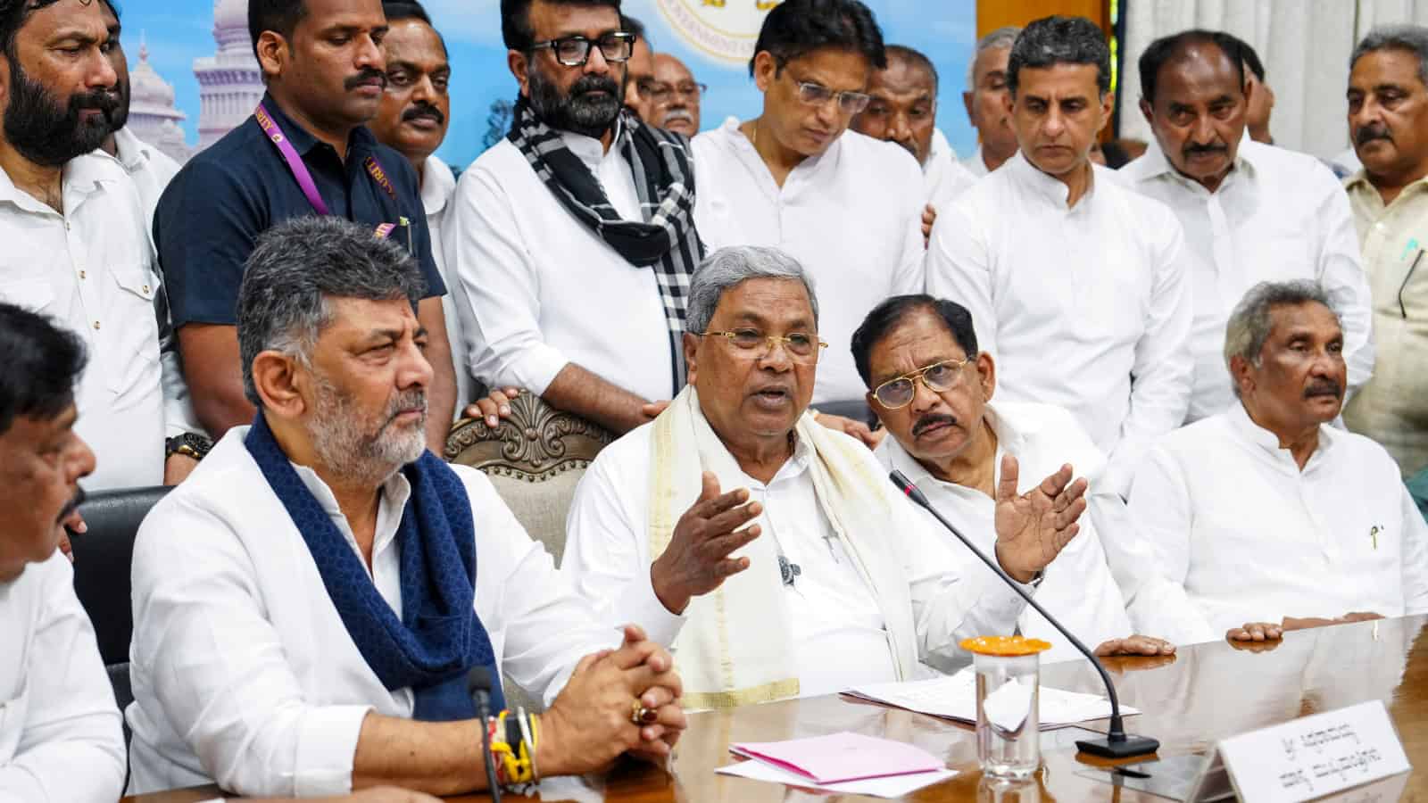 Prominent Indian politician speaking at a press conference with colleagues and media in the background.