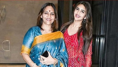 Two women smiling and posing together at a cultural event, one in a blue saree and the other in a red dre.