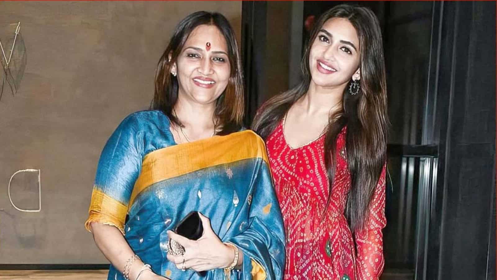 Two women smiling and posing together at a cultural event, one in a blue saree and the other in a red dre.