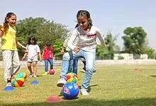 Children playing with colourful balls during summer camp activities outdoors.