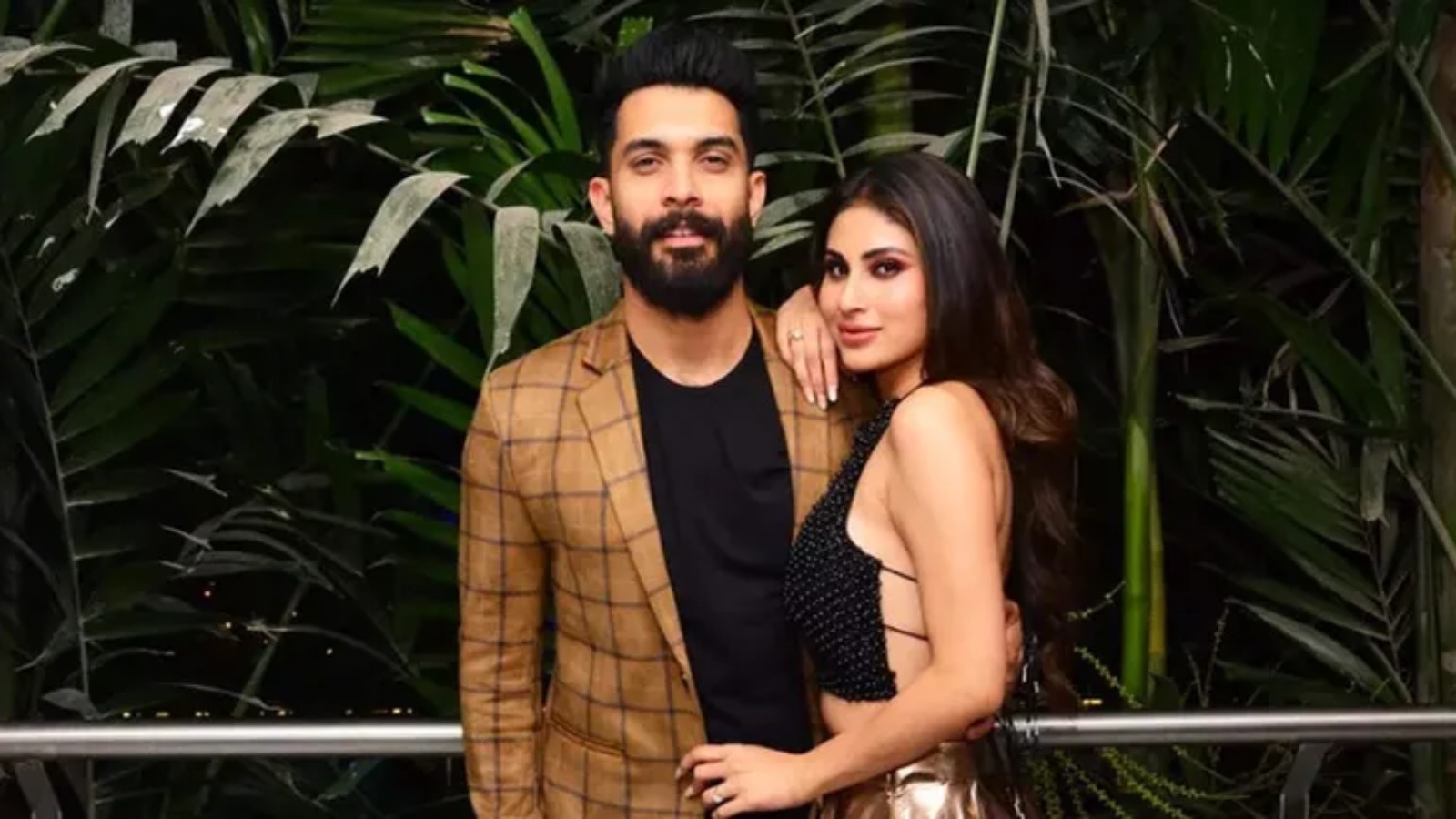A stylish man and woman posing together at The Siasat Daily event, surrounded by lush green plants.