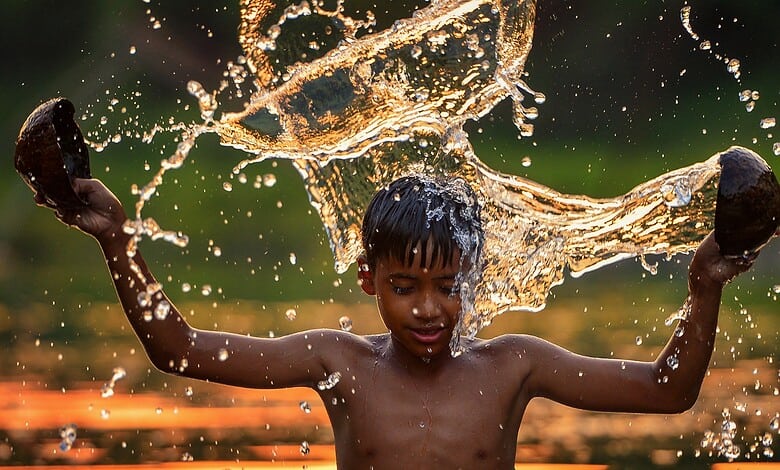 A young boy playing in water, splashing and enjoying outdoor water activity in a natural setting.