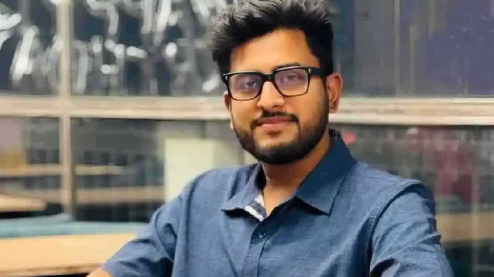 Young man wearing glasses and a blue shirt in a contemporary office environment.