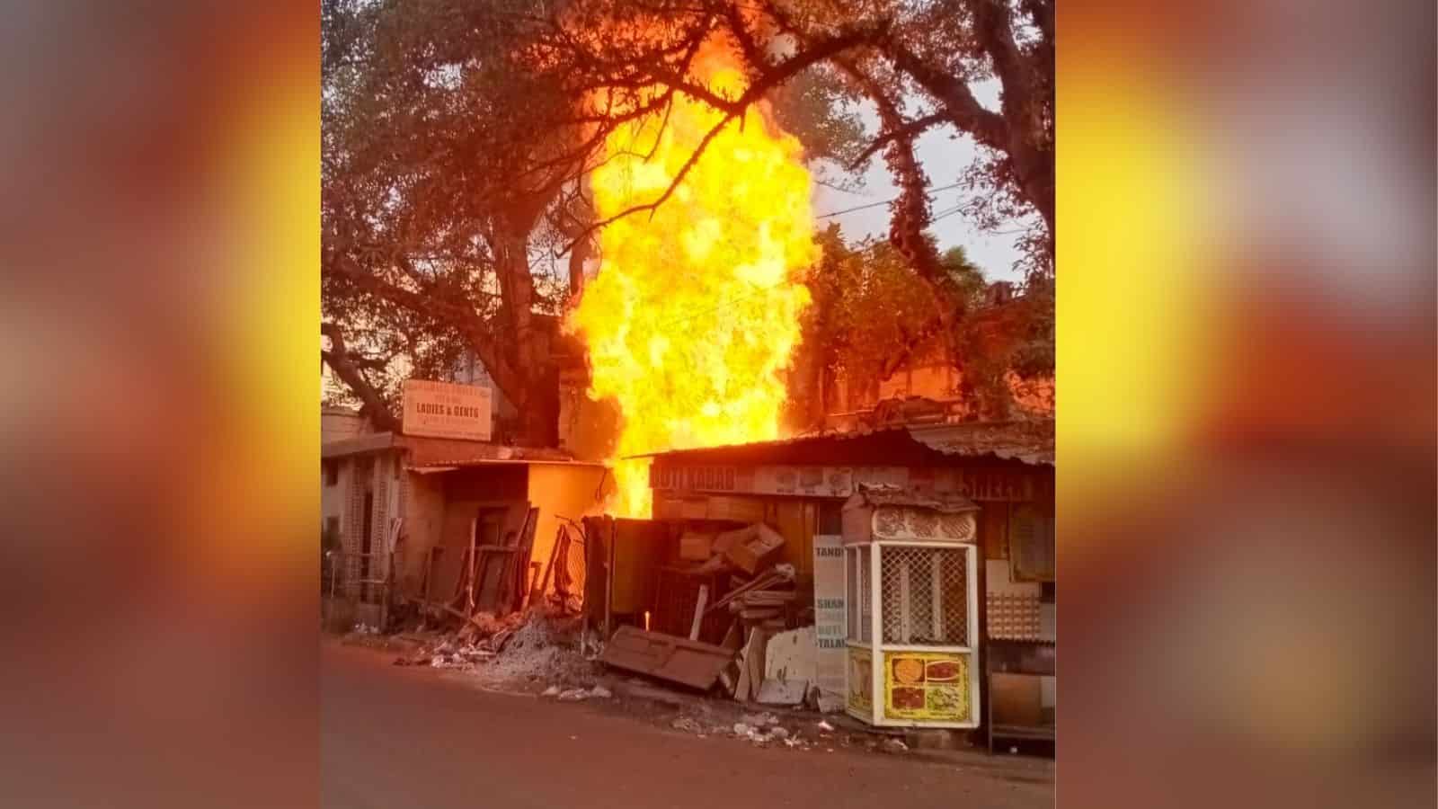 Fire erupting from a building with trees in the background during daytime, causing significant damage and.