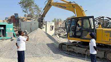 Excavator demolishing a structure at a construction site in an urban area.